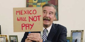 Vicente Fox holds a sign bearing a message for Trump regarding the border wall.