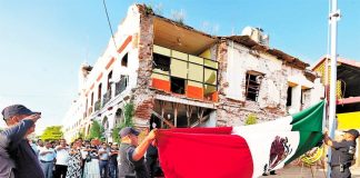 Against a backdrop of earthquake damage, Juchitán flag is lowered to half mast to mark the quake's anniversary.
