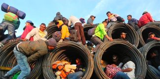 Migrants ride on a truckload of steel rolls.