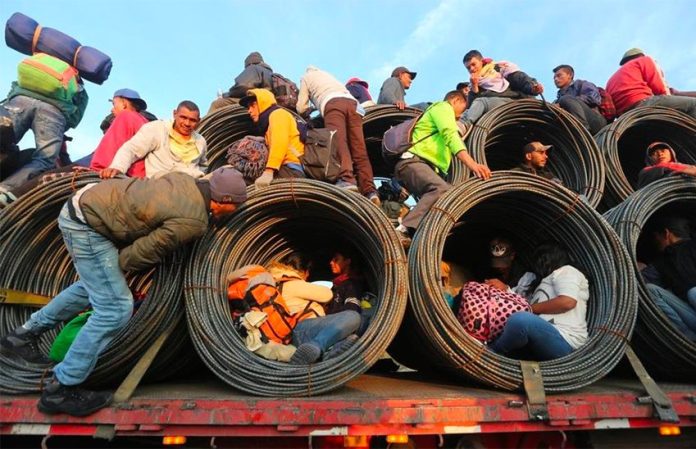 Migrants ride on a truckload of steel rolls.