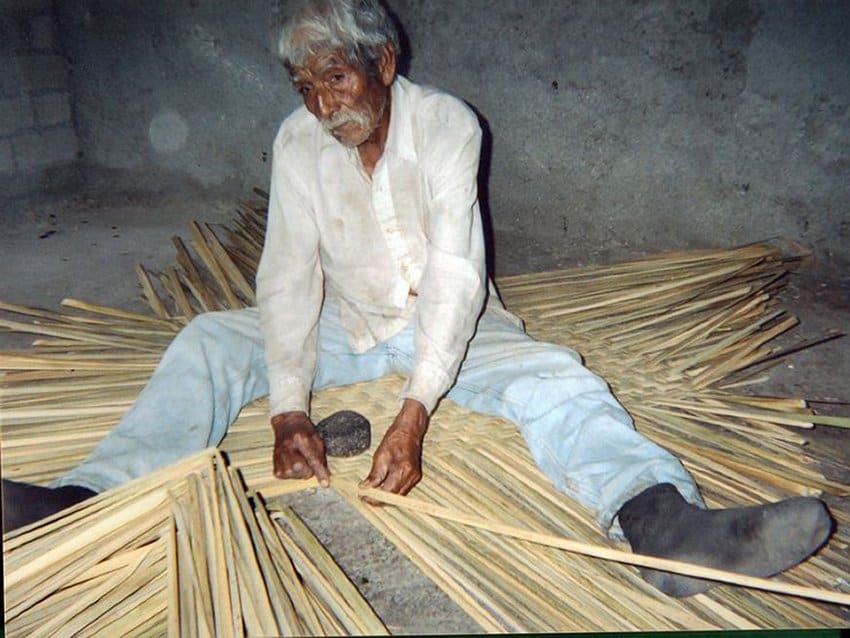 An artisan weaves a reed mat using only a stone and a metal knife.