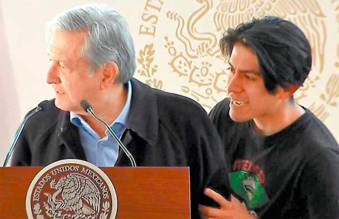 The young man who breached AMLO's security stands with the president on the stage.