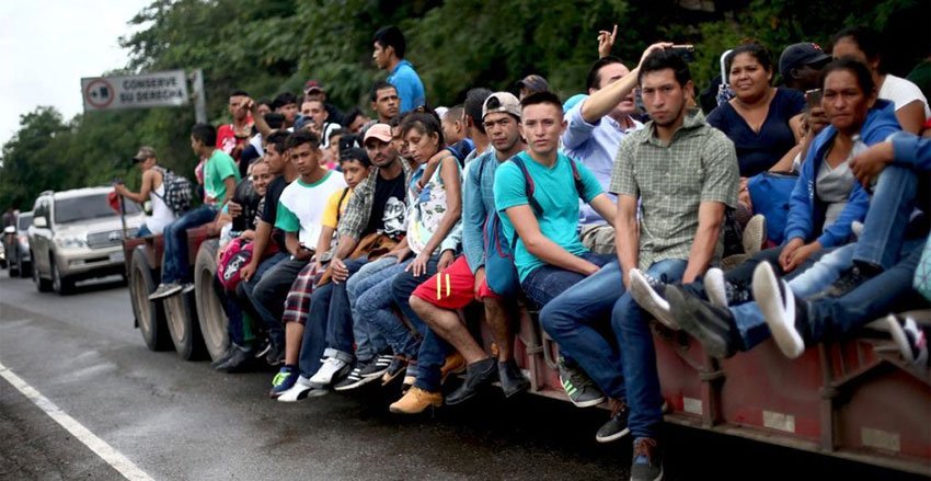Migrants hitch a ride on a trailer.