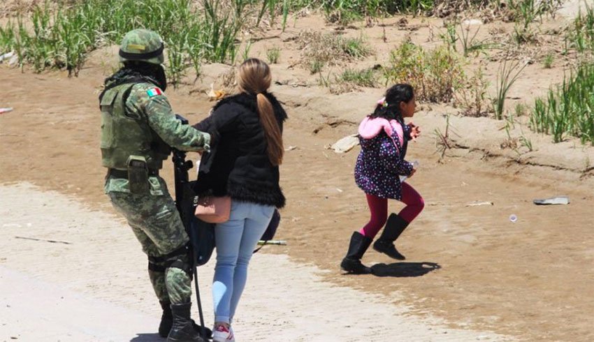 A soldier holds on to a woman while a girl appears to make a run for it.