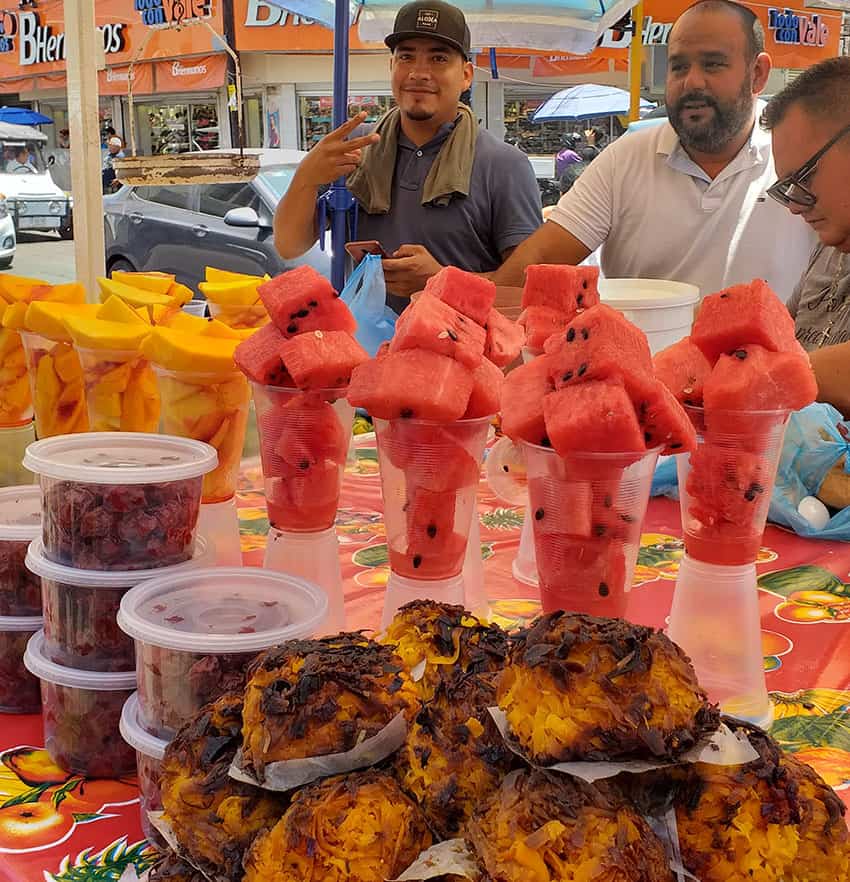 A vendor sells cups full of fresh fruit and more.