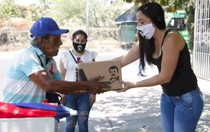 A woman hands out provisions bearing the image of the convicted drug trafficker.