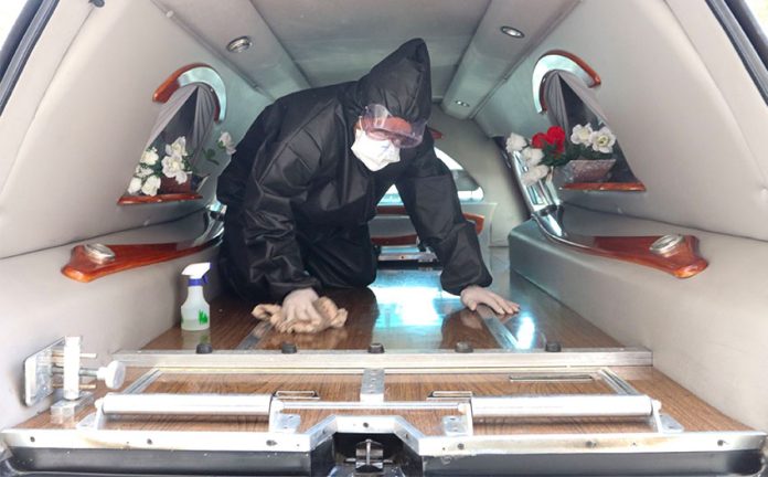 A funeral home worker disinfects a hearse.
