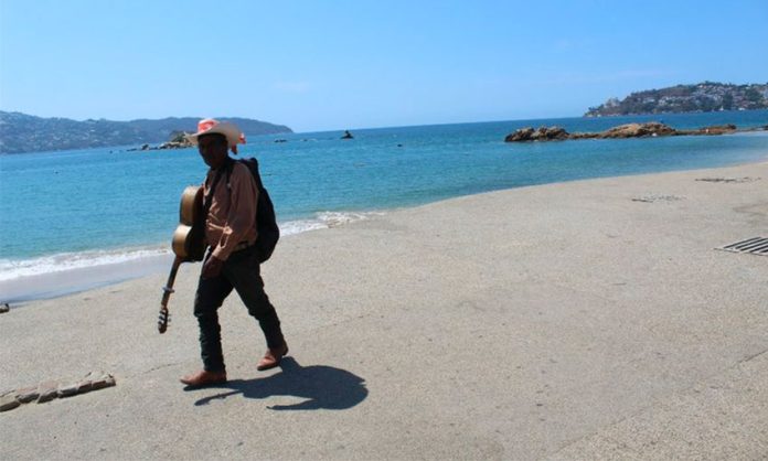 A lone musician seeks customers on a deserted Acapulco beach.