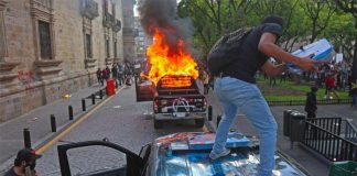A protester vandalizes a police vehicle before it was set on fire Thursday in Guadalajara.