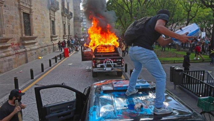 A protester vandalizes a police vehicle before it was set on fire Thursday in Guadalajara.