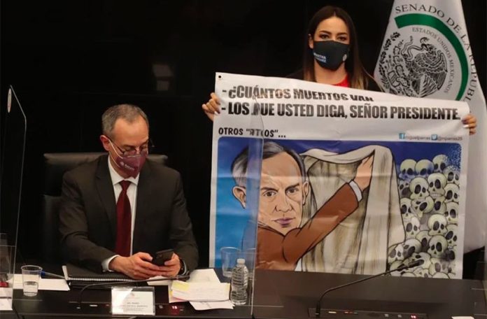A senator holds a cartoon of López-Gatell, left, during his appearance in the Senate.