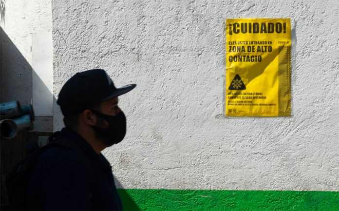 A man walks by a sign in Mexico city warning that the area is high risk for Covid contagion.