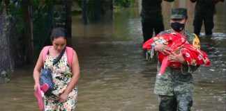 A soldier helps a woman and her child escape flooding in Tabasco.