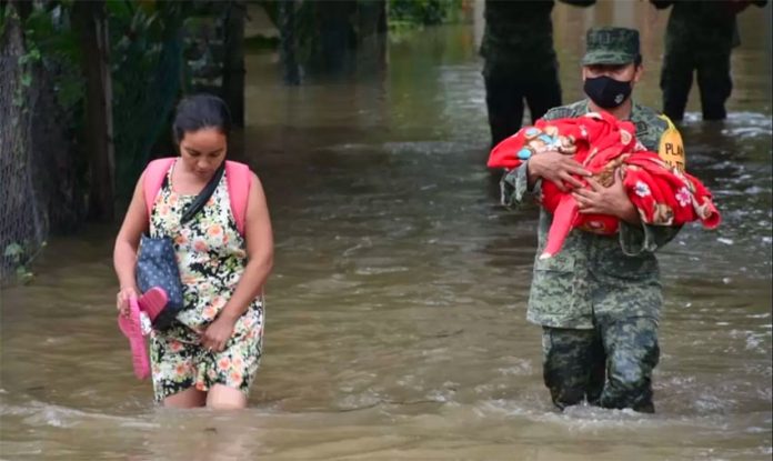 A soldier helps a woman and her child escape flooding in Tabasco.