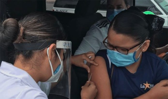 A healthcare worker administers a flu shot to a passenger in a car in Chihuahua.