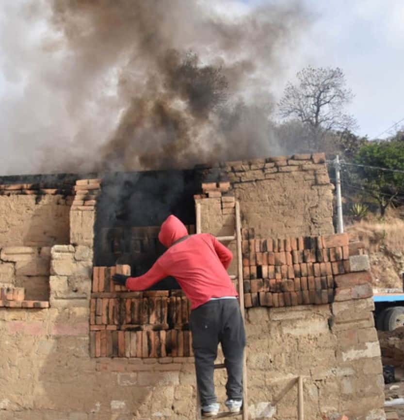 Gabino Noselo's grandson, Adolfo, seals the oven's door with unfired bricks.