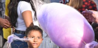 A boy watching a cotton candy vendor captures wisps of floating sugar on his stick.