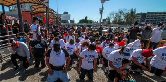 Migrants in Tijuana kneel at the border