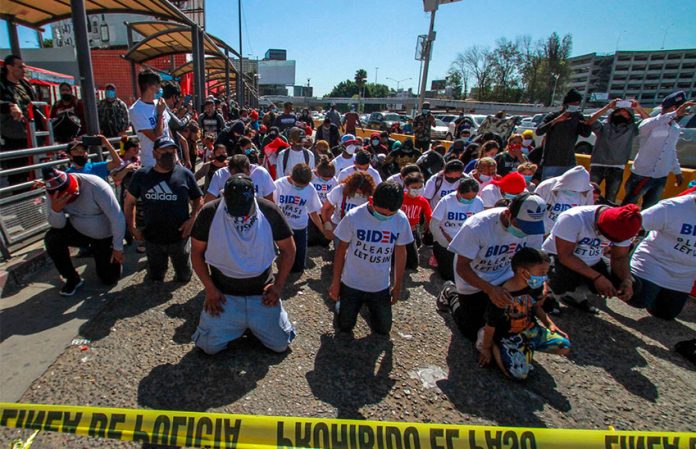 Migrants in Tijuana kneel at the border