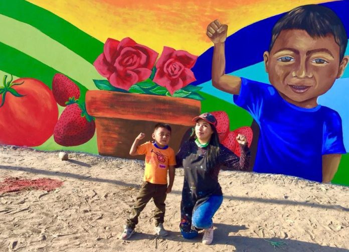 Artist Julia Celeste with budding painter Edgar in front of a mural in the Las Misiones neighborhood of San Quintín, depicting principal crops of the Valley.