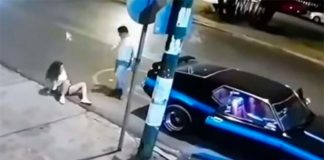 The woman sits on the road after being pushed out of the car.