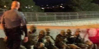 The soldiers sit at the roadside, under guard by border patrol agents.