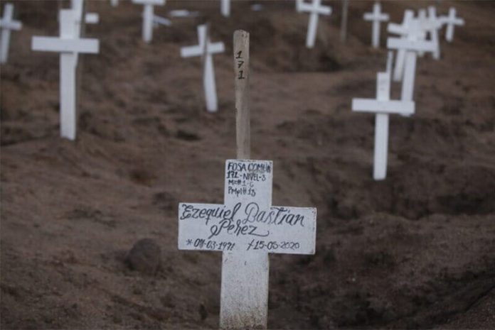 A man's name written in marker on the white cross that adorns a mass grave