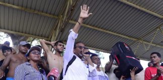Pastor and migrant advocate Luis Rey García Villagrán shouts into a microphone in a crowded area shaded by a tin roof