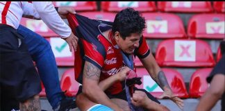 A spectator in a red Atlas jersey fights another man wearing the blue and white of the Querétaro team.