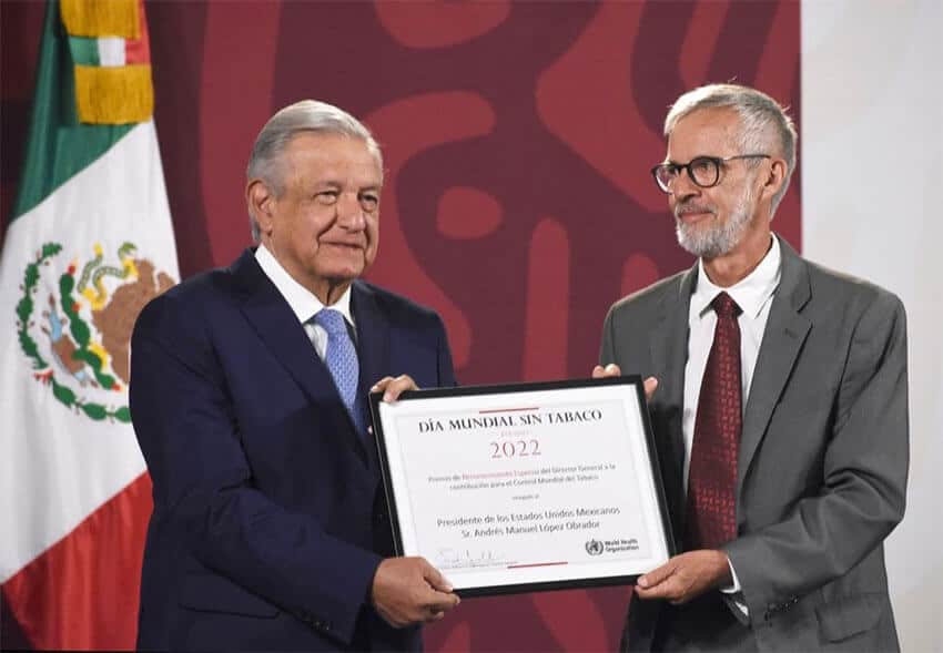 A World Health Organization representative presents President López Obrador with a recognition of his work to combat tobacco comsumption.