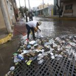 A city employee collects trash from a clogged storm drain.