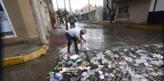 A city employee collects trash from a clogged storm drain.