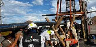 Rescue workers outside El Pinabete mine, propping up a water pipe with logs, while a government Sinaproc official looks on.