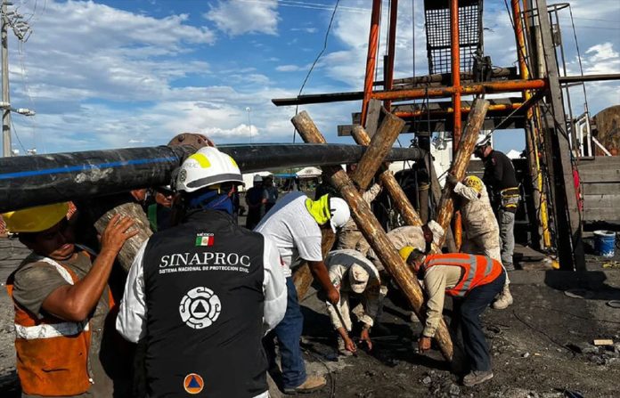 Rescue workers outside El Pinabete mine, propping up a water pipe with logs, while a government Sinaproc official looks on.