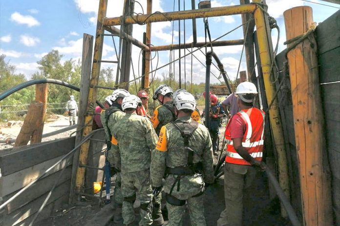 Rescue workers gather around the entrance to the mine on Sunday as water is pumped out.