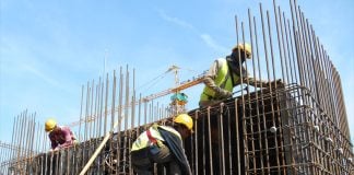 Construction workers on a rebar structure with a construction crane in the background.