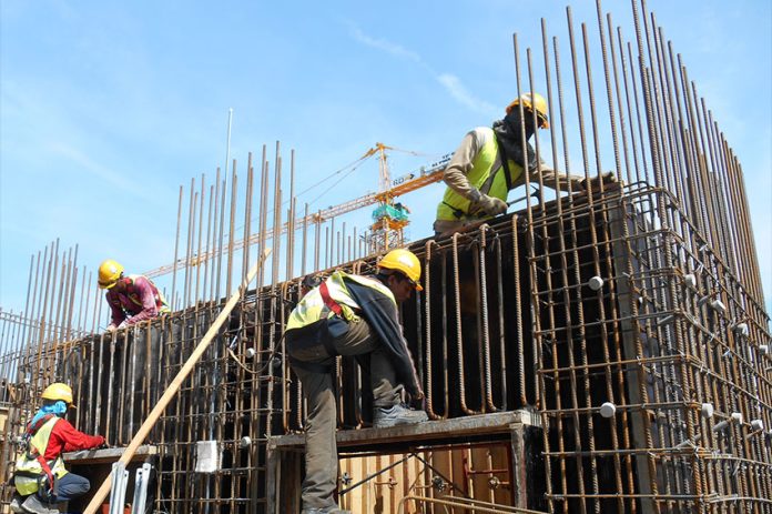 Construction workers on a rebar structure with a construction crane in the background.