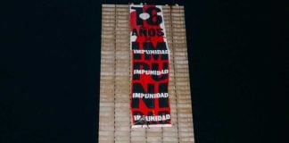 A member of the search collective Hasta Encontrarte unfurls the banner on Mexico City's Estela de Luz monument.