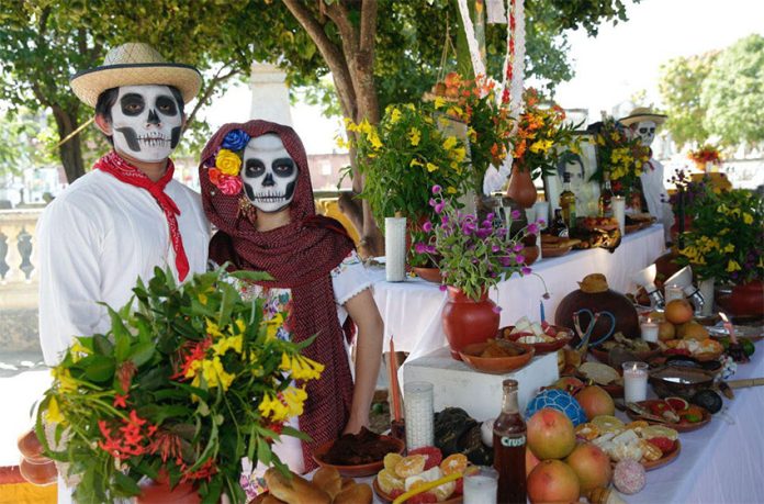 Festival participants dressed as a catrina and a catrín pose with an altar.