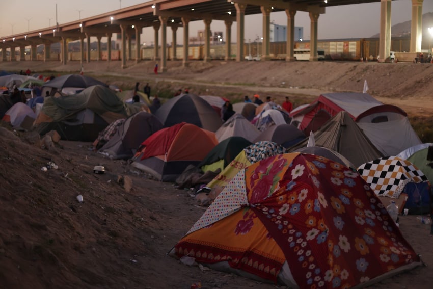 Colorful but worn tents in front of the Rio Grande, with a highway overpass in the background.