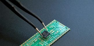 Tweezers hold a surface mounted semiconductor device over a printed circuit board, as if about to mount the device on the board.