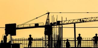 The silhouette of construction workers and a crane against a yellow sky.