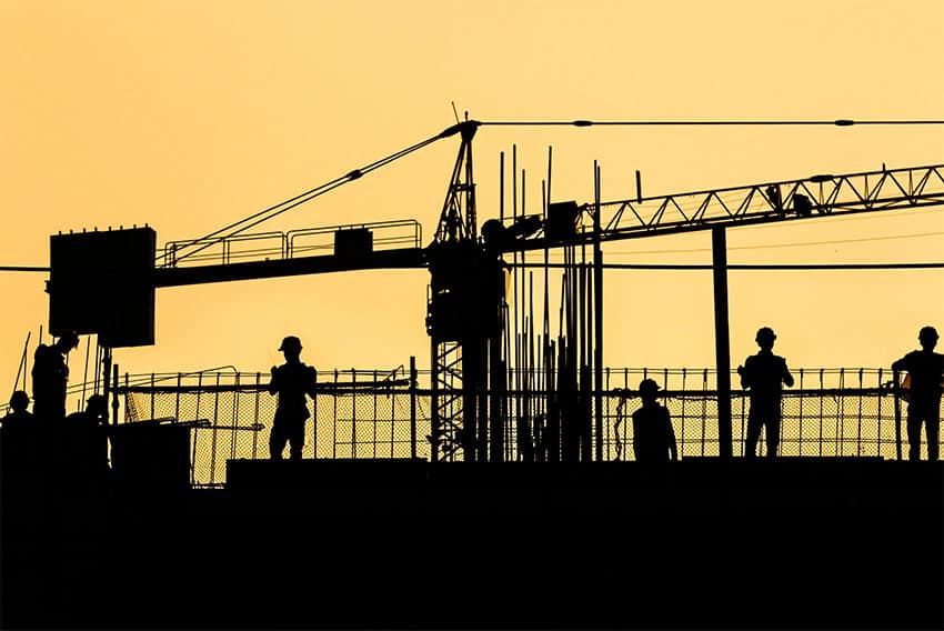 The silhouette of construction workers and a crane against a yellow sky.