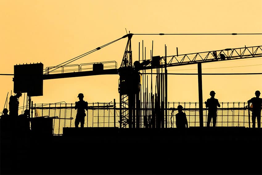 La silueta de los trabajadores de la construcción y una grúa contra un cielo amarillo.