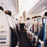A well-lit aisle inside an airplane with people seated, seen from the back of the plane.