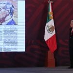 The president stands onstage on the right side, looking toward the left where there is a projected image of a newspaper article including a courtroom sketch of Genaro García Luna.