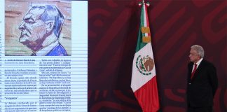 The president stands onstage on the right side, looking toward the left where there is a projected image of a newspaper article including a courtroom sketch of Genaro García Luna.