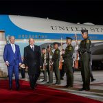 López Obrador and Biden walk away from the Air Force 1 down a red carpet with military cadets standing at attention with rifles on both sides of the walkway.