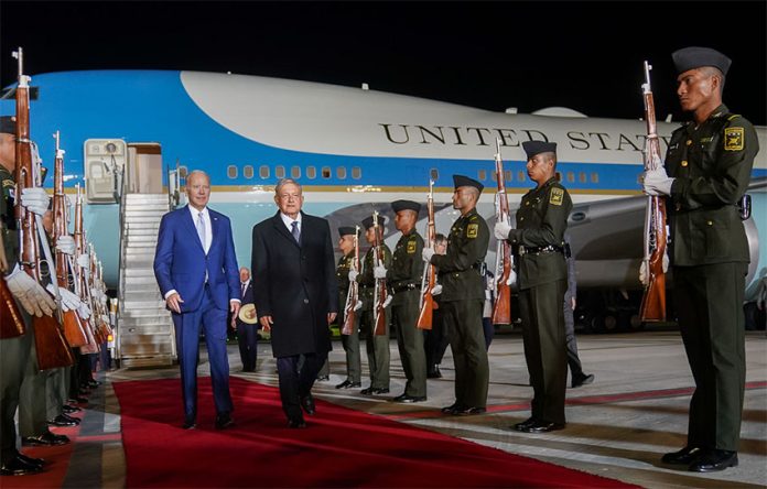 López Obrador and Biden walk away from the Air Force 1 down a red carpet with military cadets standing at attention with rifles on both sides of the walkway.