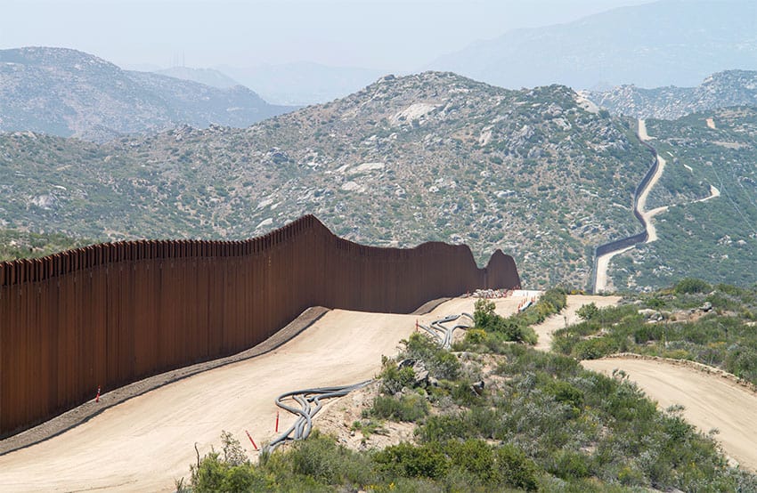 A view of the border wall between Mexico and the U.S., with the wall stretching over a hill into the distance.